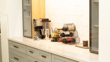 Una cocina con encimera blanca, cafetera, enfriador de vino y estante para vinos.
