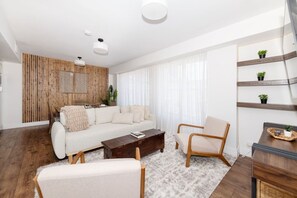 Ein modernes Wohnzimmer mit einer Couch, Sesseln, einem Couchtisch und einer Wand im Holzdesign.