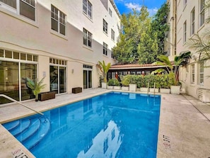 A swimming pool with steps leading into it, surrounded by a building with multiple windows and potted plants. - Newly Renovated Coastal Style Retreat South Beach (Miami Beach)