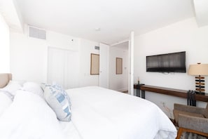 Ein Hotelzimmer mit einem großen Bett, einem an der Wand montierten Fernseher, einem Schreibtisch mit Lampe und einem Sessel.