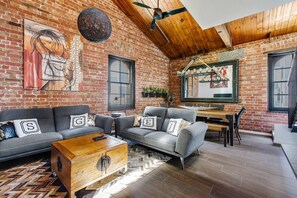 Ein geräumiges Wohnzimmer mit Backsteinwand, Holzboden und einem Essbereich inklusive Tisch und Stühlen.