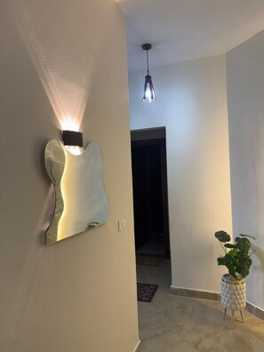 Um corredor com luminária em formato de guitarra fixada na parede, luminária pendente e um vaso de planta.