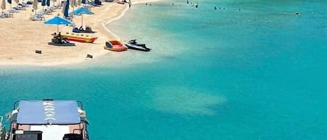 A coastal resort with a sandy beach, clear turquoise waters, and a row of multi-story buildings in the background.