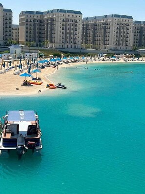 A coastal resort with a sandy beach, clear turquoise waters, and a row of multi-story buildings in the background.