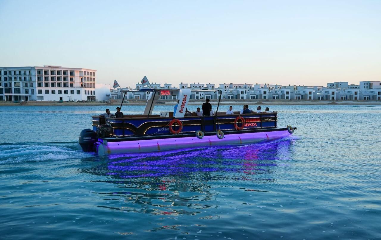 Een boot met de naam 'ABAZA' op de zijkant, die over het water vaart met een stadsgezicht op de achtergrond.