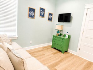 Ein Zimmer mit einem beigen Sofa, einem grünen Schminktisch und drei gerahmten Kunstwerken an der Wand.