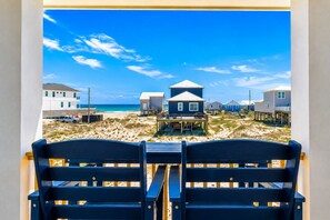 Blick auf einen Strand vom Balkon aus, mit zwei blauen Stühlen, einem Haus mit weißem Dach und einem sandigen Strand im Hintergrund.