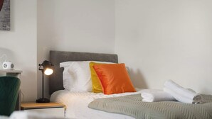 A hotel room with a neatly made bed, a bedside lamp, a power strip, and a green chair. - Cozy 2BR Home Sleeps 5 with WiFi by Stay With Us (Platt Bridge)