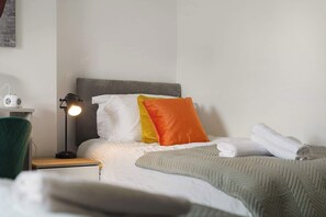 Ein Hotelzimmer mit einem ordentlich bezogenen Bett, einer Nachttischlampe, einer Steckleiste und einem grünen Sessel.