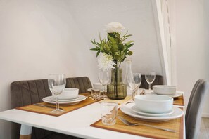 A dining table set with white plates, bowls, and glasses, accompanied by a vase with white flowers and green foliage. - Cozy 2BR Home Sleeps 5 with WiFi by Stay With Us (Platt Bridge)