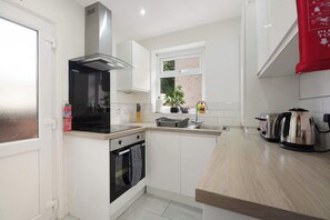 A modern kitchen with white cabinetry, a stainless steel range hood, a built-in oven, and a window providing natural light. - Cozy 2BR Home Sleeps 5 with WiFi by Stay With Us (Platt Bridge)