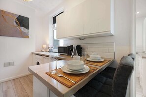 Une cuisine moderne avec des meubles blancs, un four à micro-ondes encastré et un coin repas doté d’une table en bois, mise pour deux personnes.