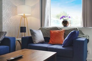 Un salon comprenant un canapé, une table basse, une lampe et une fenêtre donnant sur l’extérieur.