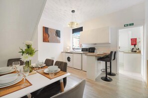 A modern kitchen with a dining area, a washing machine, and a fire exit sign. - Cozy 2BR Home Sleeps 5 with WiFi by Stay With Us (Platt Bridge)