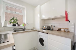 A modern kitchen with a built-in washing machine, a sink, and a window with a plant. - Cozy 2BR Home Sleeps 5 with WiFi by Stay With Us (Platt Bridge)