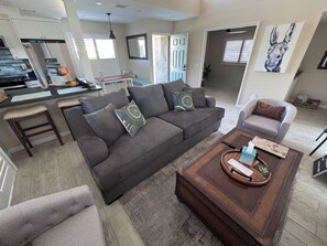 A modern living room with a grey sofa, a coffee table, and a dining area with a kitchen in the background.