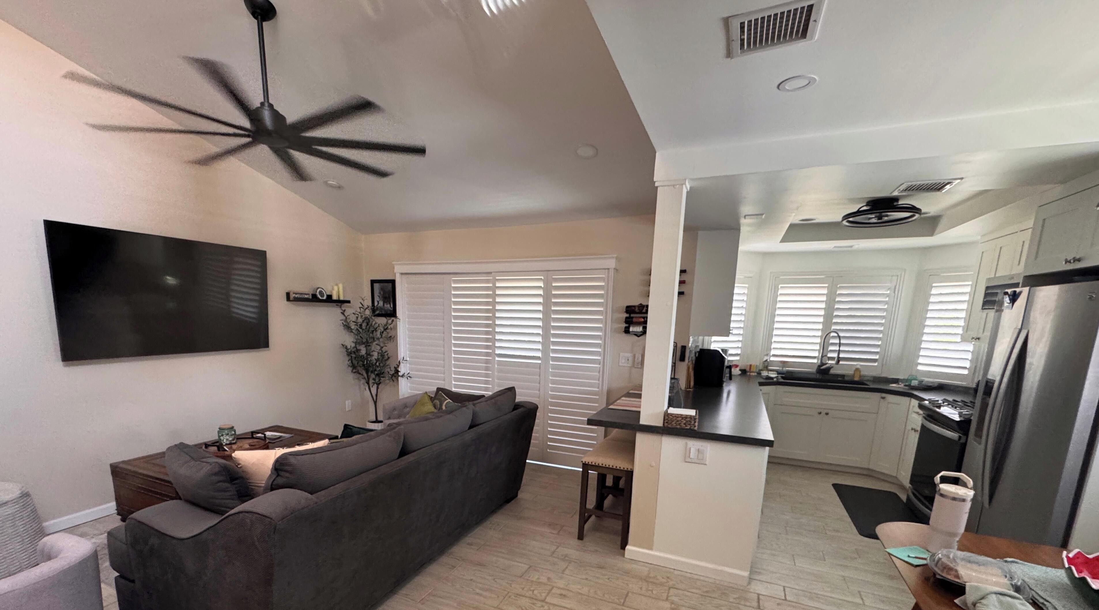 A modern living room with a grey sofa, a ceiling fan, and a flat-screen TV.