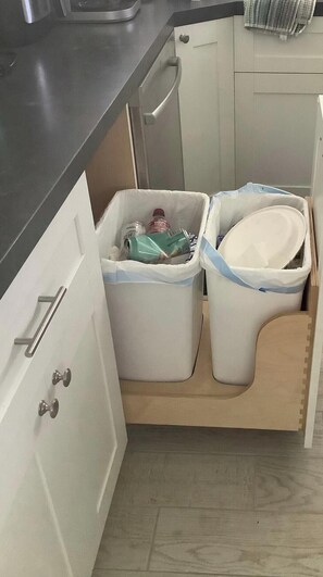 Eine Küche mit weißen Schränken, einer schwarzen Arbeitsplatte und zwei Mülleimern.
