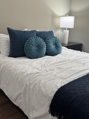 Un lit bien fait, avec une couette blanche et deux coussins décoratifs.