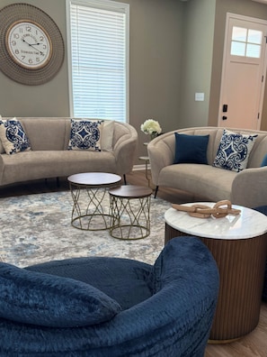 A living room with two sofas, round coffee tables, and a decorative wall clock. - THE COBALT-NEW, Beautiful 3 bed/2.5bath Townhome @ Oxford Commons, 2 car garage (Oxford)