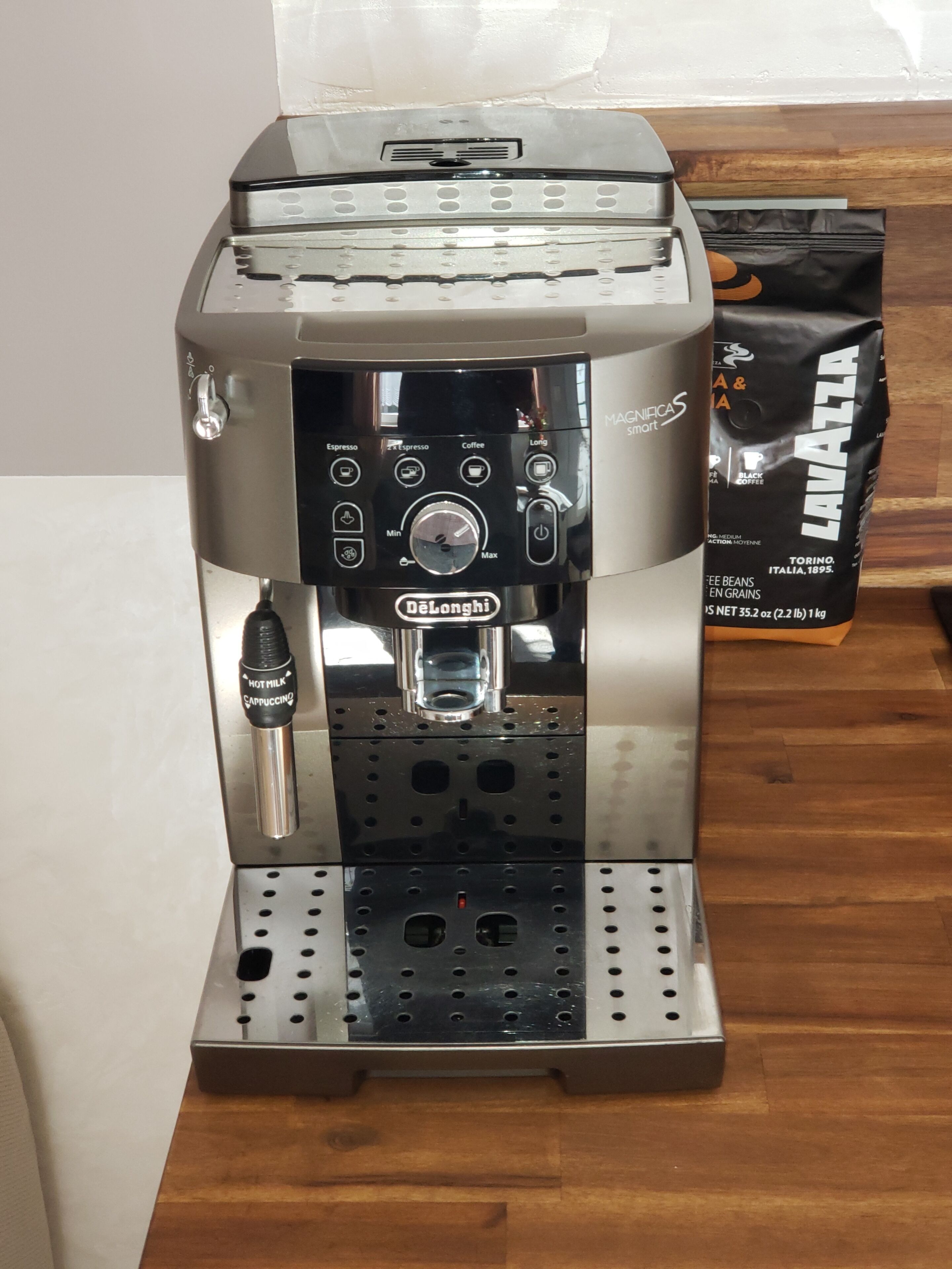 A De'Longhi espresso machine with a milk frother attachment, a coffee bag, and a wooden floor.
