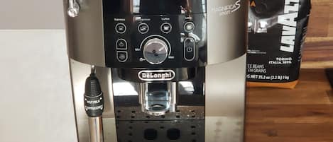 A De'Longhi espresso machine with a milk frother attachment, a coffee bag, and a wooden floor.