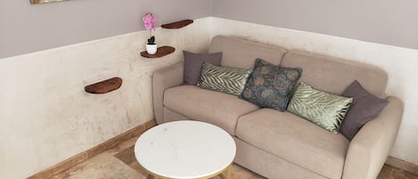A corner room with a beige sofa, a small round table, and a potted plant.