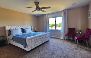 A bedroom with a large bed, a ceiling fan, a window with curtains, and two chairs. - Sterling Heights Retreat ! (Sterling Heights)
