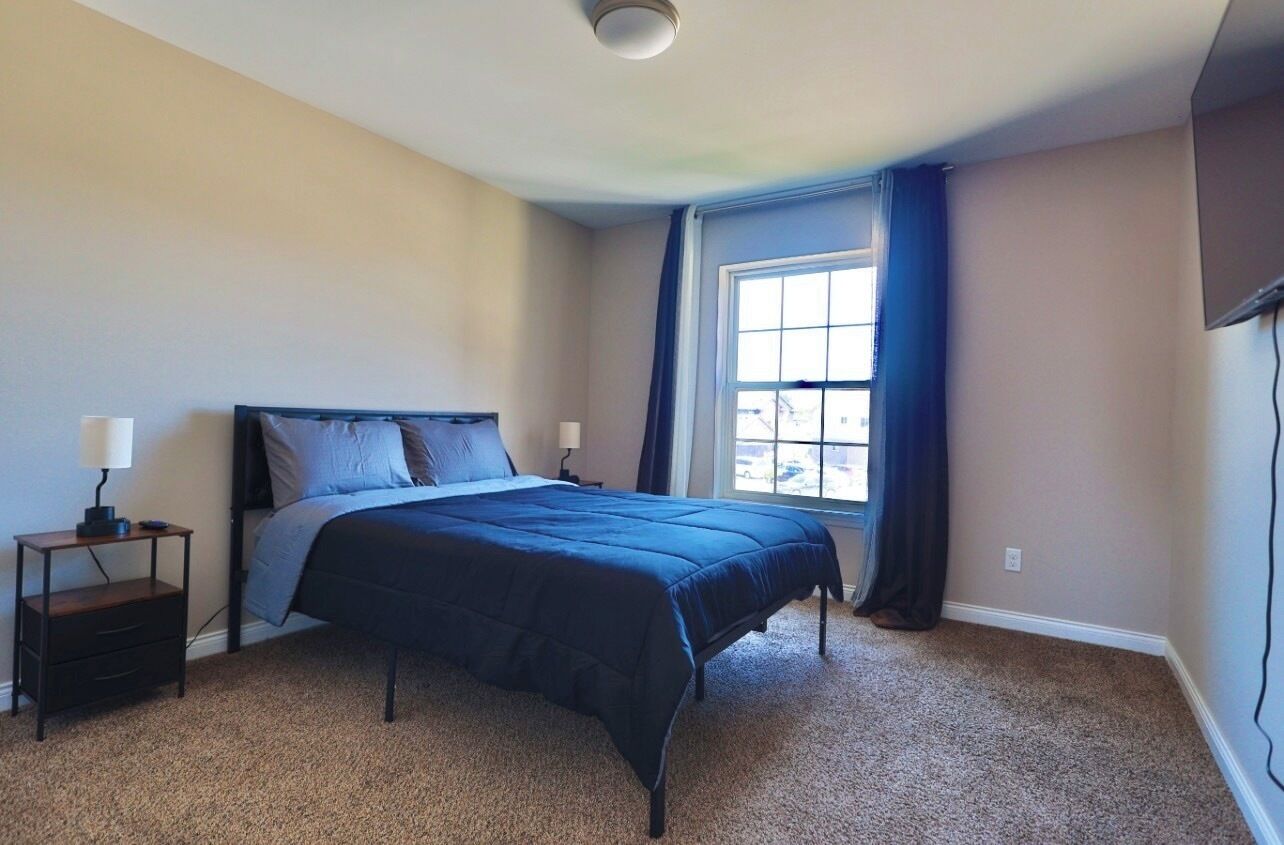 A bedroom with a bed, a nightstand, a window with curtains, and a ceiling light.
