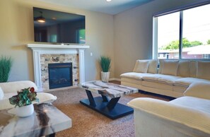 A living room with a fireplace, a sofa, a coffee table, and a TV mounted above the fireplace. - Sterling Heights Retreat ! (Sterling Heights)