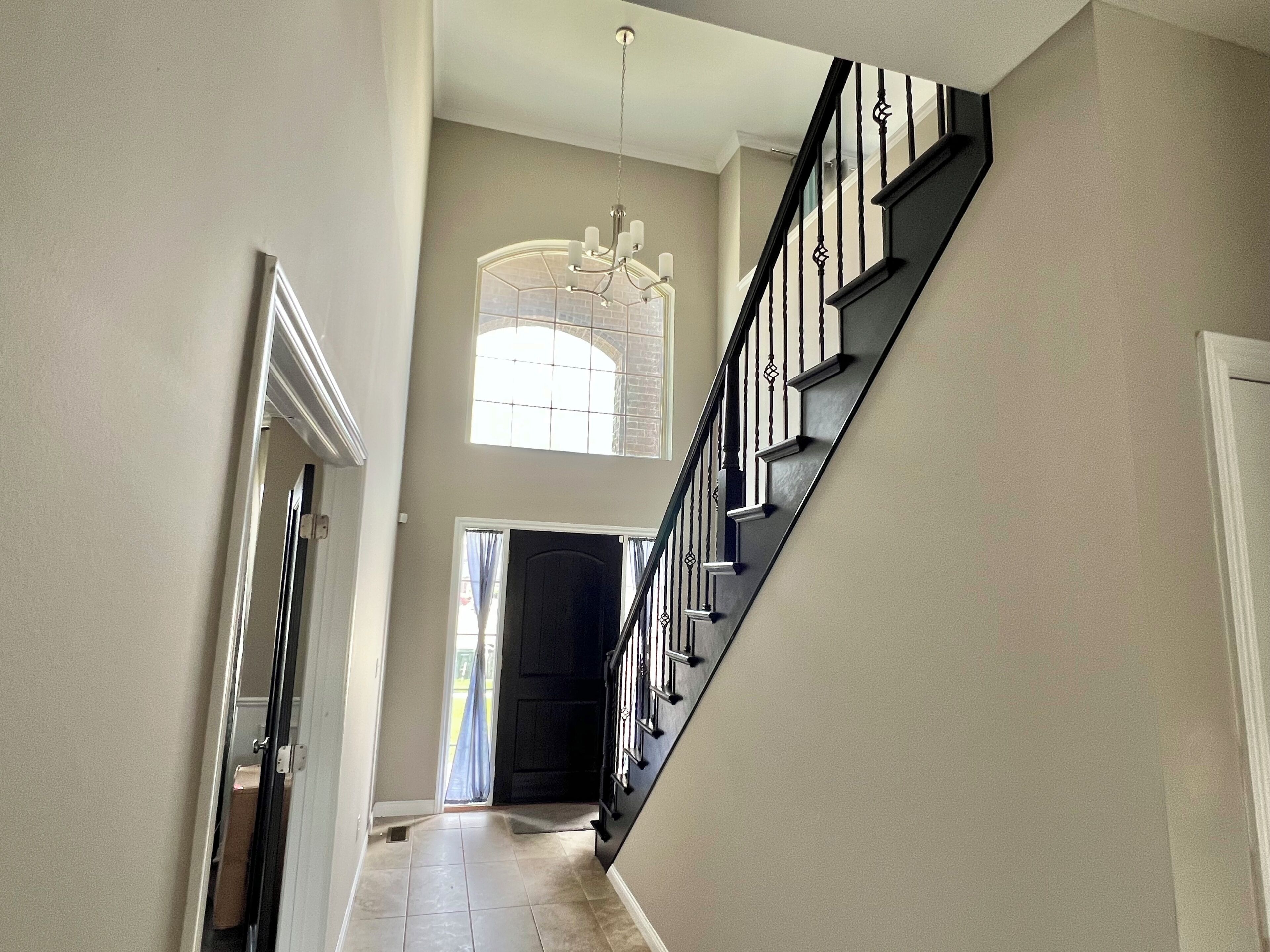 A staircase with a black railing and a chandelier in the hallway.