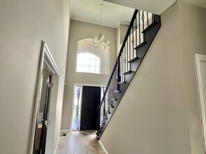 A staircase with a black railing and a chandelier in the hallway. - Sterling Heights Retreat ! (Sterling Heights)