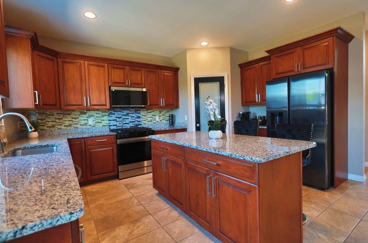 Cocina con gabinetes de madera, encimeras de granito, electrodomésticos de acero inoxidable y salpicadero de azulejos.
