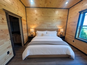 Ein Schlafzimmer mit Holzvertäfelung, einem großen Bett, zwei Nachttischen mit Lampen und einem Fenster.