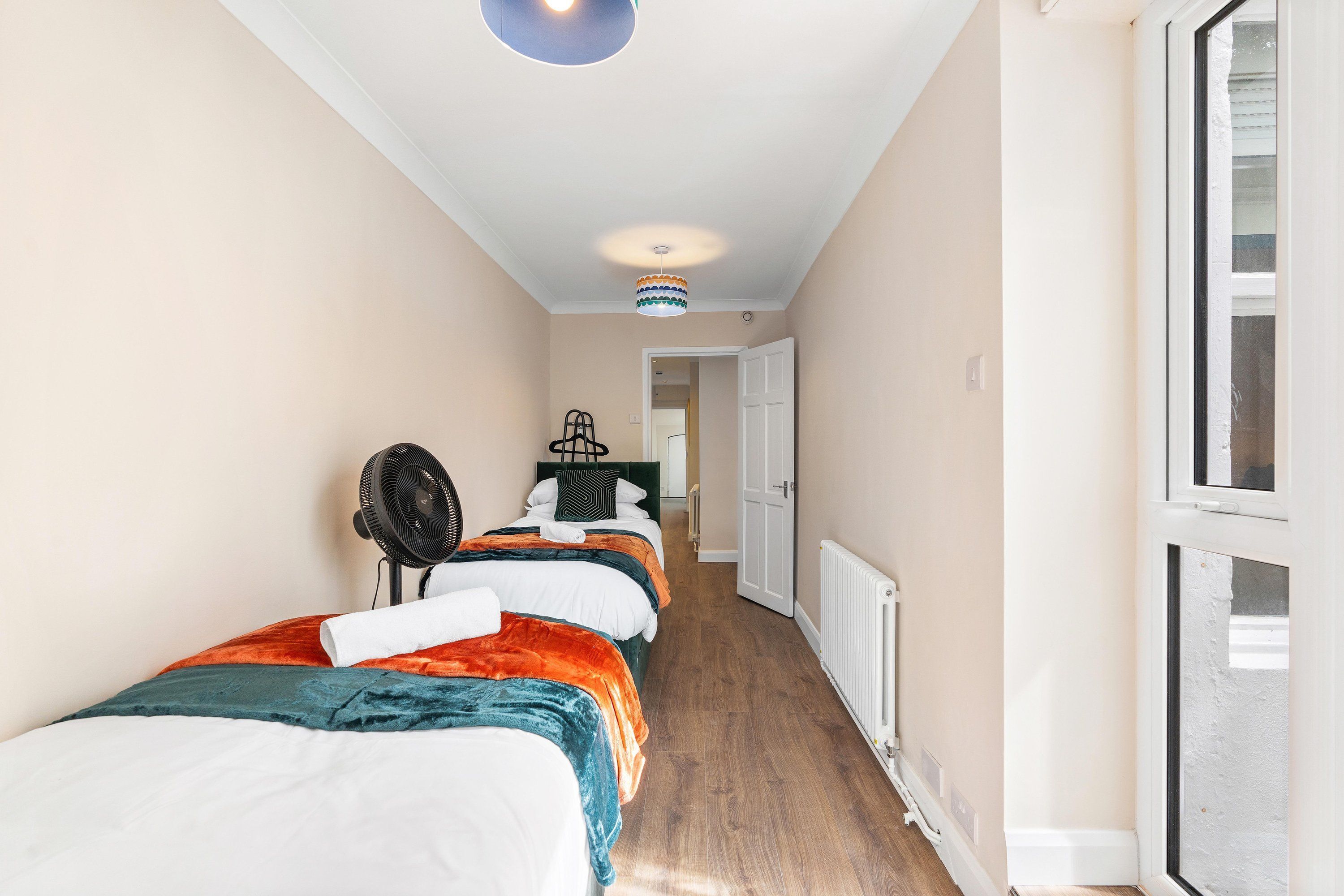 A narrow hallway with a bed on the left, a radiator on the right, and a door at the end.