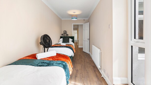 A narrow hallway with a bed on the left, a radiator on the right, and a door at the end. - Coastal Calm By My Getaways (Brighton)