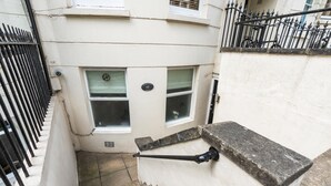 A narrow stairway leading to a flat with a white exterior wall, a black metal fence, and a window with a metal grate. - Coastal Calm By My Getaways (Brighton)