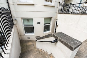 A narrow stairway leading to a flat with a white exterior wall, a black metal fence, and a window with a metal grate. - Coastal Calm By My Getaways (Brighton)