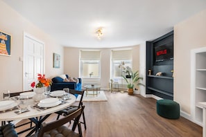 A modern living space with a dining area, a sofa, a TV, and a bookshelf. - Coastal Calm By My Getaways (Brighton)