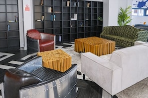 Ein moderner Lounge-Bereich mit einem schwarzen Bücherregal, einem roten Ledersessel, einem gemusterten grünen Sofa, einem weißen Couchen und einem Holztisch.