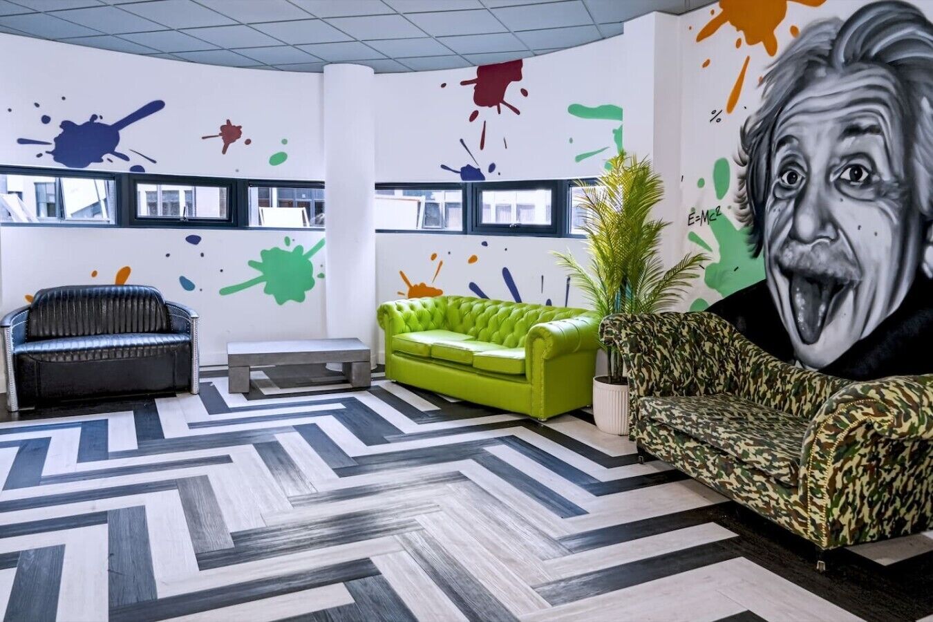 Un interior modern amb un sofà verd, un canapè de cuir negre i una butaca estampada.