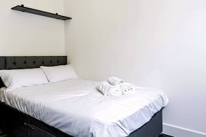 Ein Bett mit weißen Leinen, einem dunklen Kopfteil und zusammengerollten Handtüchern daneben.