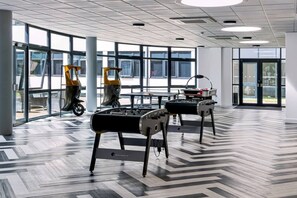 Eine großzügige Lobby mit modernem Design, inklusive einem gemusterten Boden, großen Fenstern und zwei Tischfußballtischen.