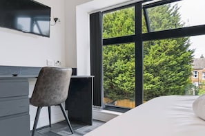 Un dormitorio con cama, escritorio y silla. Hay una ventana con vistas a árboles.