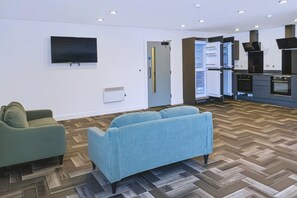 Een moderne woonkamer met een flatscreen televisie, een bank en een keukenhoek met een inbouwoven en magnetron.