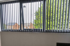 A window with vertical bars and a chain top, overlooking a residential area with houses and greenery. - Brand New Spacious Studio in Beeston (Beeston)