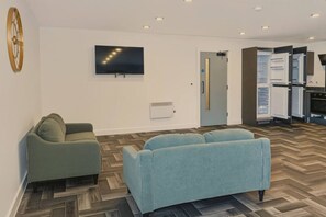 Ein modernes Wohnzimmer mit einer Couch, einem an der Wand montierten Fernseher und einer Küchenzeile mit offenem Kühlschrank.