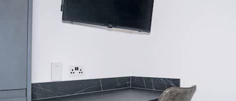 A modern room with a flat-screen TV mounted on the wall, a marble-topped table, and a chair.