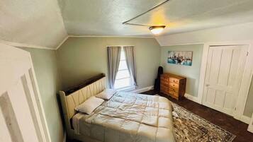 A bedroom with a bed, a dresser, a painting, and a window with curtains.