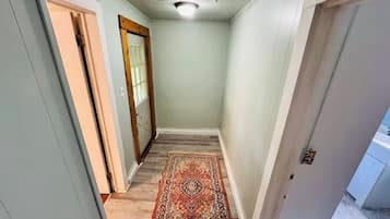 A narrow hallway with a patterned rug, a wooden door, and a white wall.